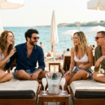 Due giovani coppie eleganti chiacchierano con champagne sui lettini di una spiaggia a Cap d'Agde