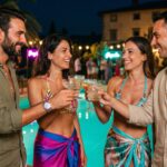 Due coppie si conoscono a un pool party notturno e brindano insieme
