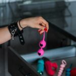 Donna in lingerie di pizzo nero che sceglie un giocattolo da un cassetto aperto con altri accessori erotici